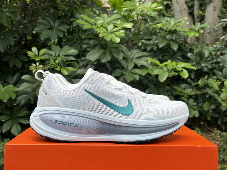 White running shoes with green accents on an orange box against a green leafy background