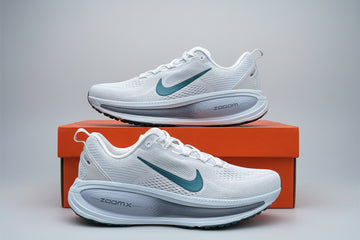 White running shoes with green accents on an orange box against a green leafy background